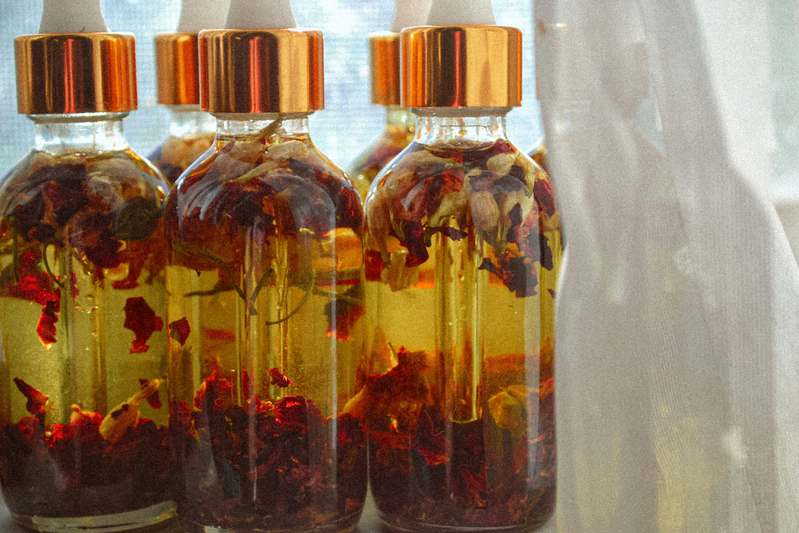 Open journal next to dried flower petals and glass jars of floral oils